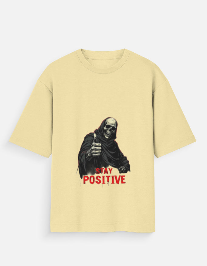 Beige t-shirt with a graphic of a skeleton holding a sign that says 'Stay Positive' on a white background.