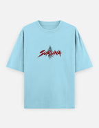 A light blue short-sleeve t-shirt with a red and black stylized 'SUKUNA' graphic printed on the chest, displayed against a light gray background.