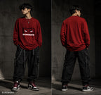 A model shown in a split front and back view wearing a red long-sleeve sweatshirt with a graphic print on the chest, black cargo pants, and sneakers, set against a dark concrete wall background. The brand name KUOWEAR is visible in the bottom-left corner.