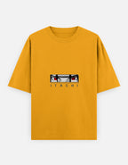 A mustard yellow short-sleeve t-shirt featuring a graphic of the anime character Itachi Uchiha's eyes and the name 'ITACHI' printed below, displayed on a light gray background.
